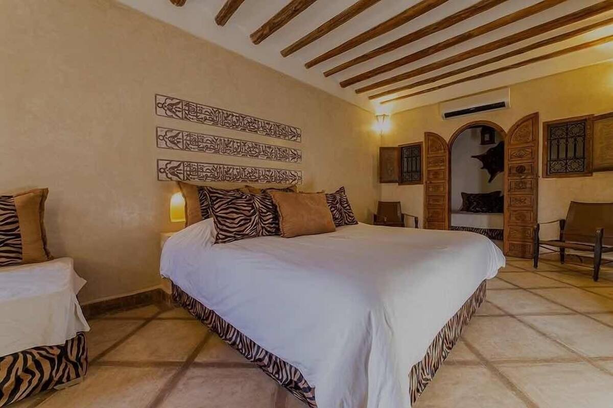 A bedroom with a large bed, a nightstand, a chair, and a decorative wall with calligraphy.