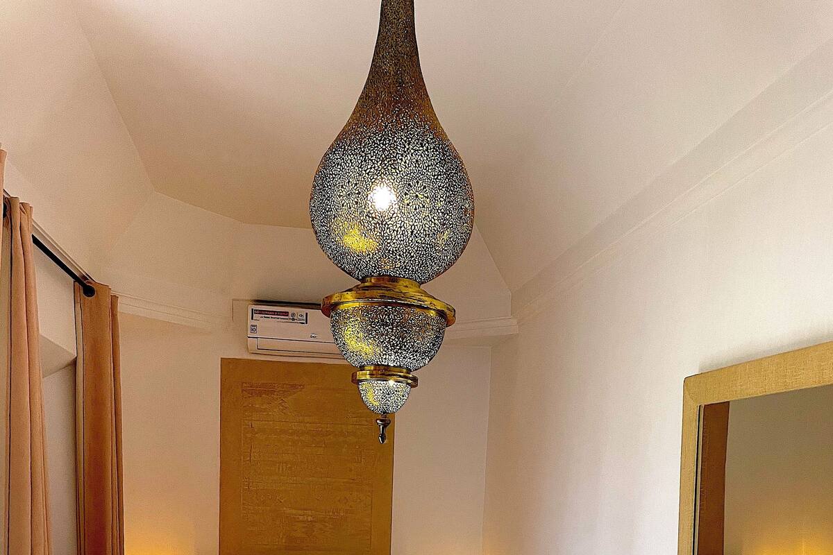 A bedroom with a bed, a sofa, a large mirror, and a hanging light fixture.