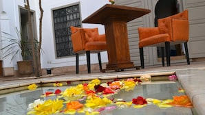 A pool with floating flower petals, a wooden table, and two orange chairs. - Riad See Moon et Spa (Marrakech)