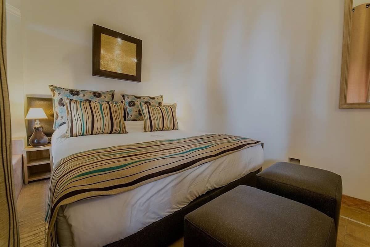 A neatly arranged bedroom with a bed, pillows, a bedside table with a lamp, and a wall-mounted picture.