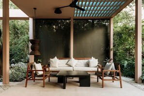 Ein ĂŒberdachter AuĂenbereich mit einer Sitzecke, die eine Couch und StĂŒhle umfasst, einem Tisch und einem Deckenventilator.