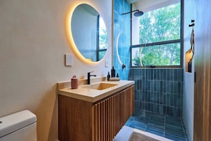 Une salle de bain moderne avec un meuble-lavabo en bois, un grand miroir, une douche avec une porte en verre et une vue sur la verdure Ă lâextĂ©rieur.