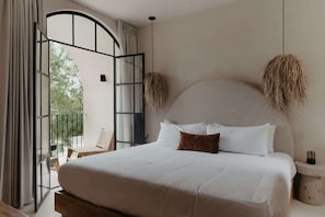 Une chambre avec un grand lit, un balcon avec des rideaux et une vue sur la verdure.