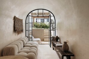 A cozy interior with a sofa, a small table with a vase, and a view through an arched doorway to an outdoor area with plants and a staircase. - Casa Zebrina Romantic Design Apartment Beach Club (Tulum)