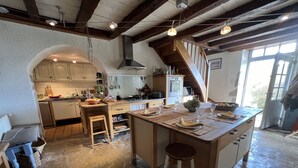 A spacious kitchen with a large island, wooden beams, and a stone floor. - Grande Maison Avec vue Exceptionnelle sur le Lot (Calvignac)