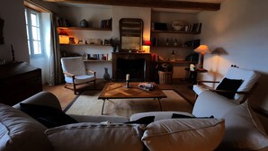 A cozy living room with a fireplace, bookshelves, a comfortable sofa, and a wooden coffee table. - Grande Maison Avec vue Exceptionnelle sur le Lot (Calvignac)