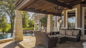 Un patio exterior con pilares de piedra, muebles de mimbre y vista a una piscina.