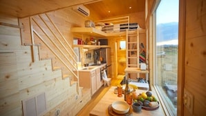 Een knus houten cabin interieur met een keukenhoek, een eettafel met servies en uitzicht door een groot raam.