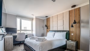 Ein modernes Hotelzimmer mit einem großen Bett, einem Schreibtisch mit Computer und Blick auf die Stadt durch das Fenster.