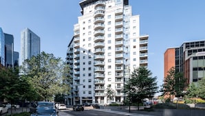 Ein modernes Hochhaus mit mehreren Balkonen, umgeben von Bäumen und anderen Gebäuden.