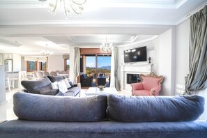 A spacious living room with a large sofa, a television, a fireplace, and a view of the outdoors.