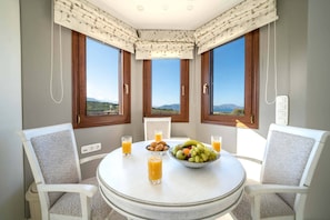 A dining area with a round table, two chairs, a bowl of fruit, and glasses of orange juice.