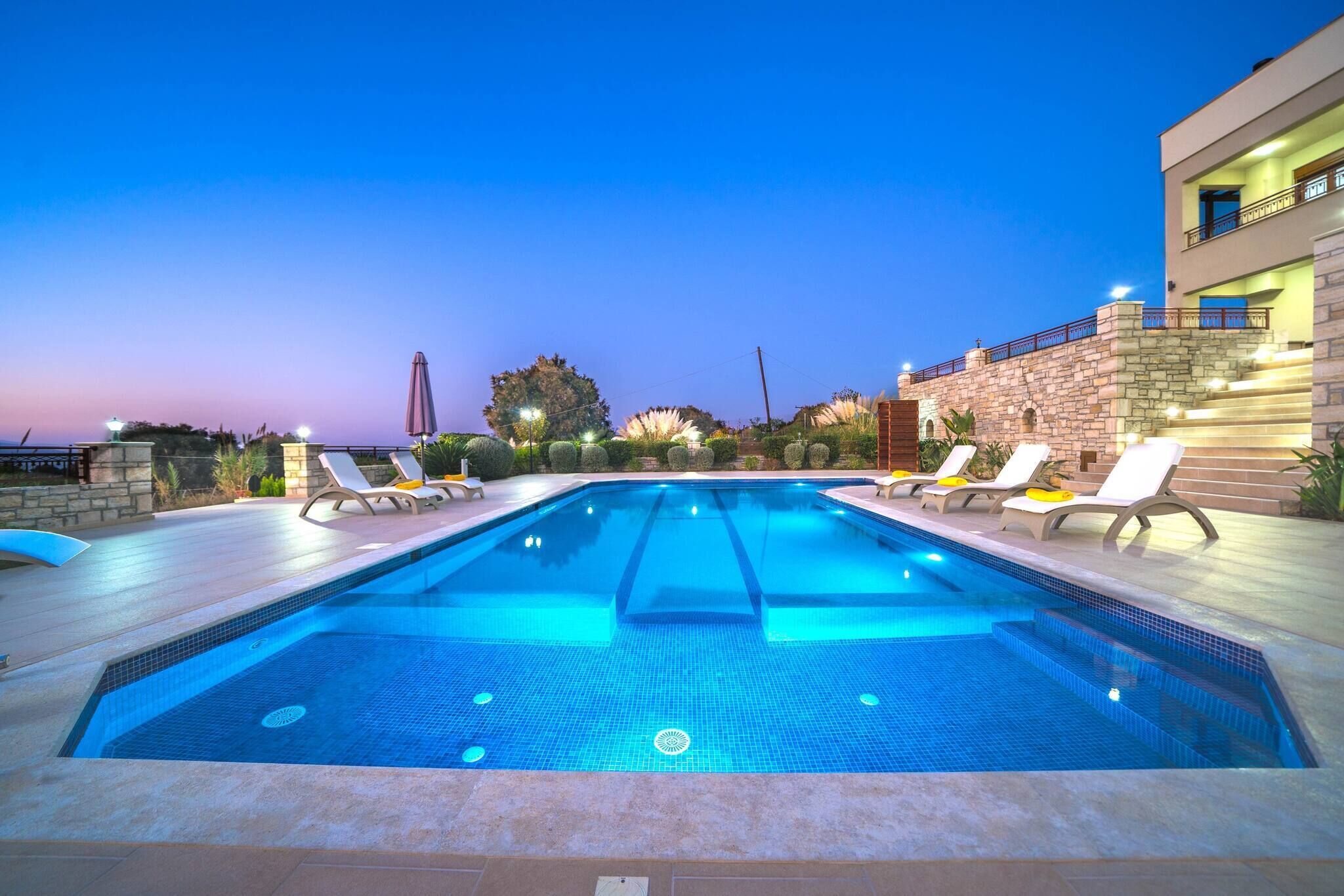 Une piscine avec des chaises longues, un mur en pierre et un bâtiment doté de balcons.