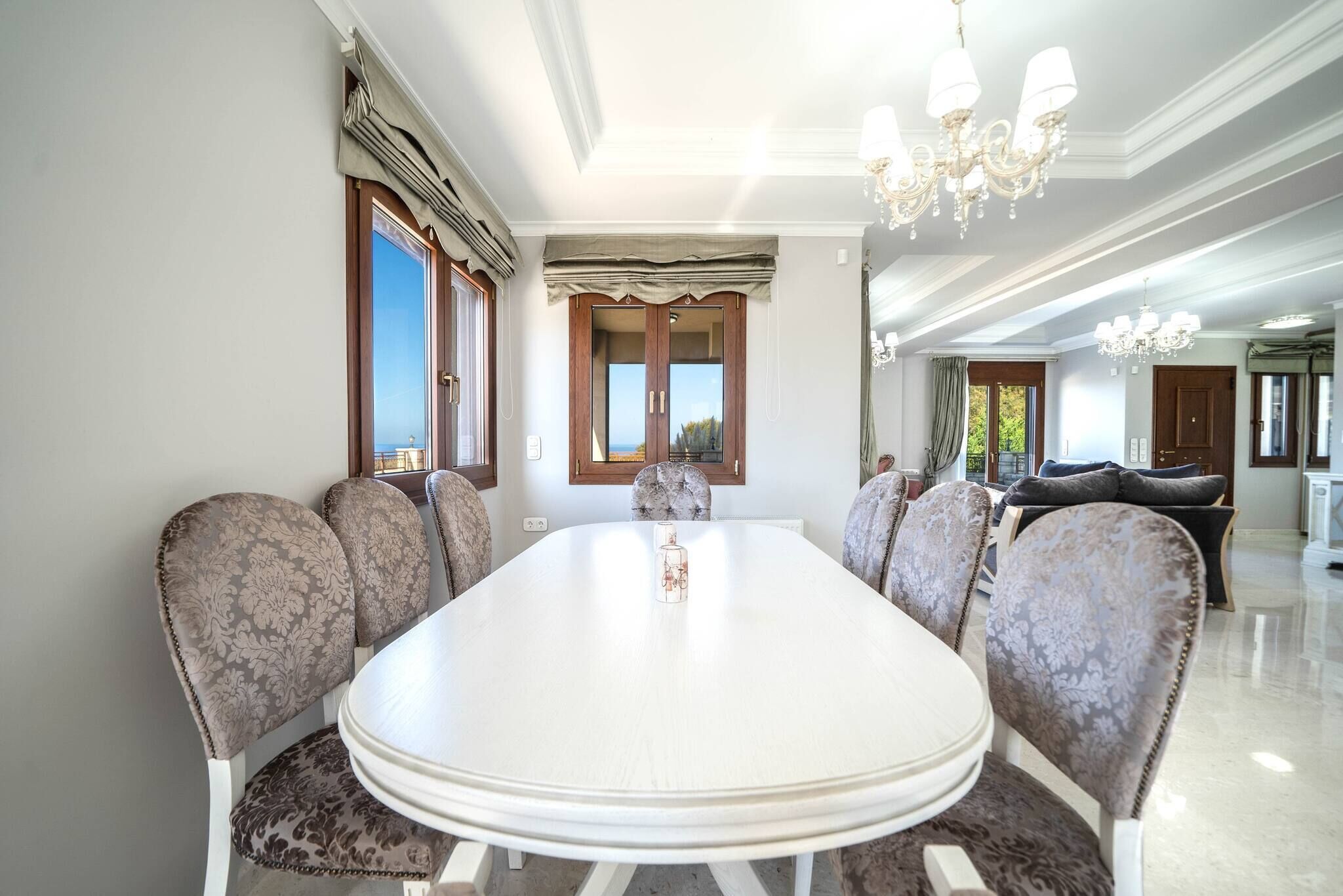 A dining room with a large oval table, patterned chairs, and a chandelier.