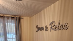 Une chambre d’hôtel avec un lit, une grande fenêtre ornée de rideaux légers et un panneau mural sur lequel on peut lire : « Rêvez et détendez-vous ».