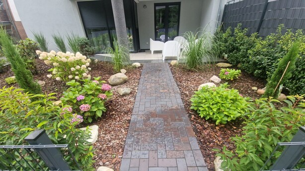 Un chemin de jardin menant à une maison moderne dotée d’un patio.