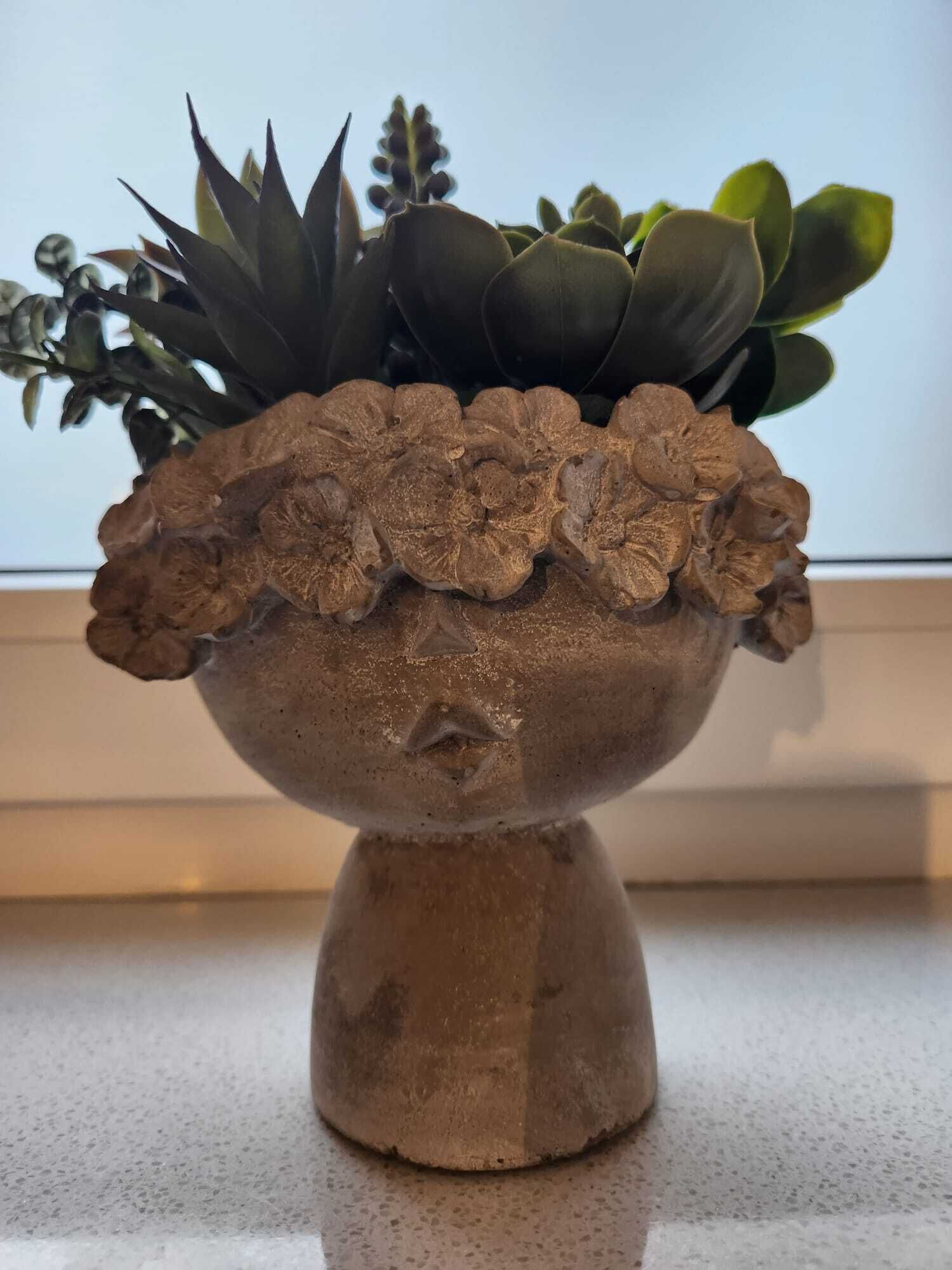 A terracotta pot with a textured design, containing green succulents and a small plant with dark green leaves.