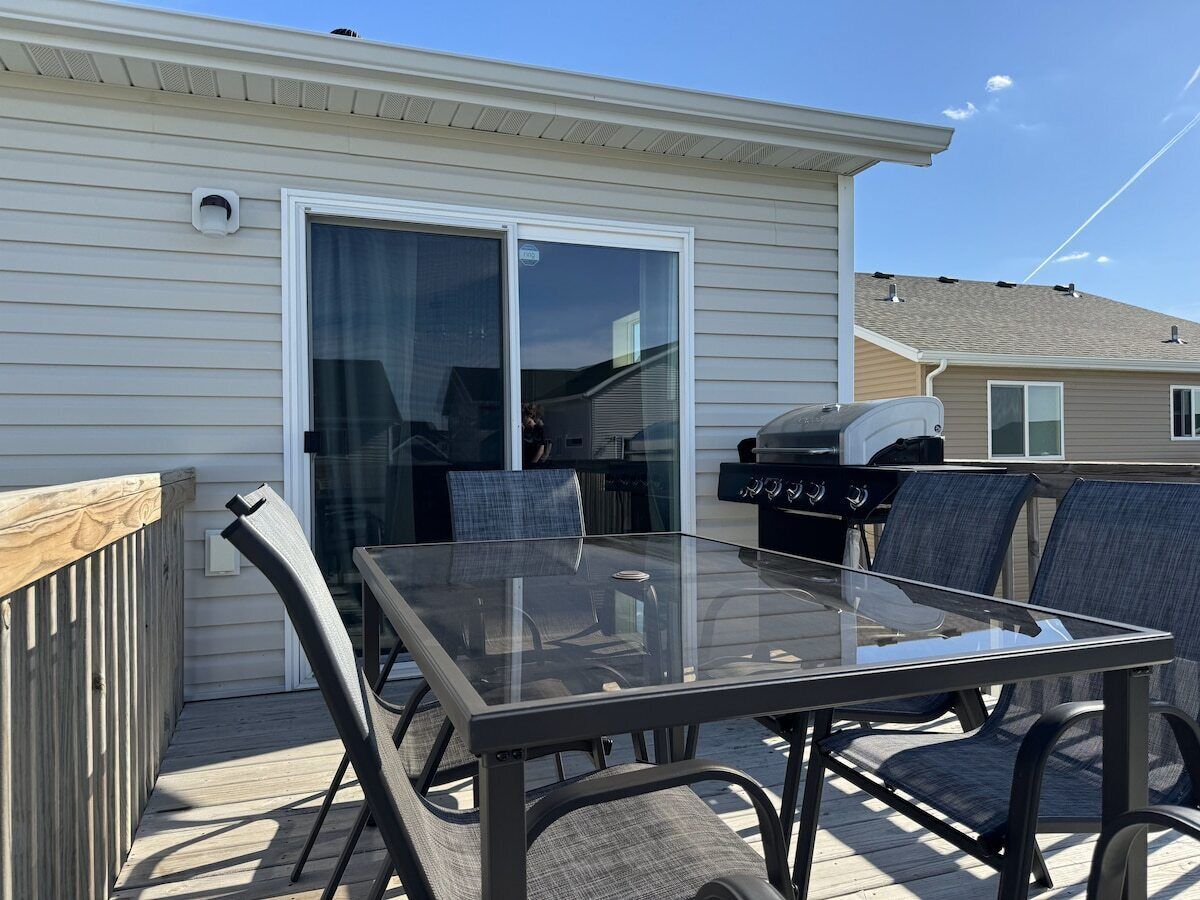 An outdoor patio with a glass-top table and chairs, a barbecue grill, and a sliding glass door leading to a covered area.