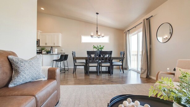 A modern living room with a brown leather sofa, a dining table with chairs, a chandelier, and a kitchen in the background. - Easy Access I29 & I94 - Family Friendly - Spacious (Fargo)