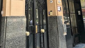 Eine Gebäudefassade mit aufwendiger Architektur, einem schwarzen Metallgitter und einem blauen Schild, das einen geschützten Bereich kennzeichnet.