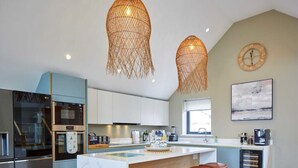 Una cocina moderna con una isla central, taburetes de bar, un refrigerador, microondas y un reloj en la pared.