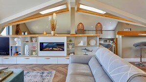 Una sala de estar moderna estilo loft con un televisor grande, estanterías empotradas y un techo alto con tragaluces.