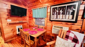A wooden cabin interior with a dining table set for four, a television mounted on the wall, and a framed picture of wine bottles. - Spectacular Views to Remember! Near hiking, biking, wineries, pet friendly (Fleetwood)