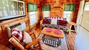 A cozy cabin interior with wooden walls and ceilings, a ceiling fan, a sofa with patterned cushions, a small table, and a refrigerator. - Spectacular Views to Remember! Near hiking, biking, wineries, pet friendly (Fleetwood)