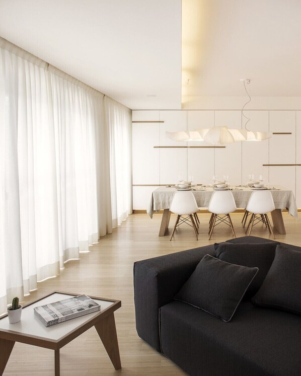 A modern living room with a dark sofa, a glass coffee table, and a dining area with a table set for four.