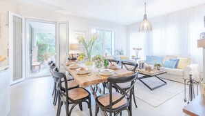 A bright dining area with a wooden table, chairs, and a sofa in the background.