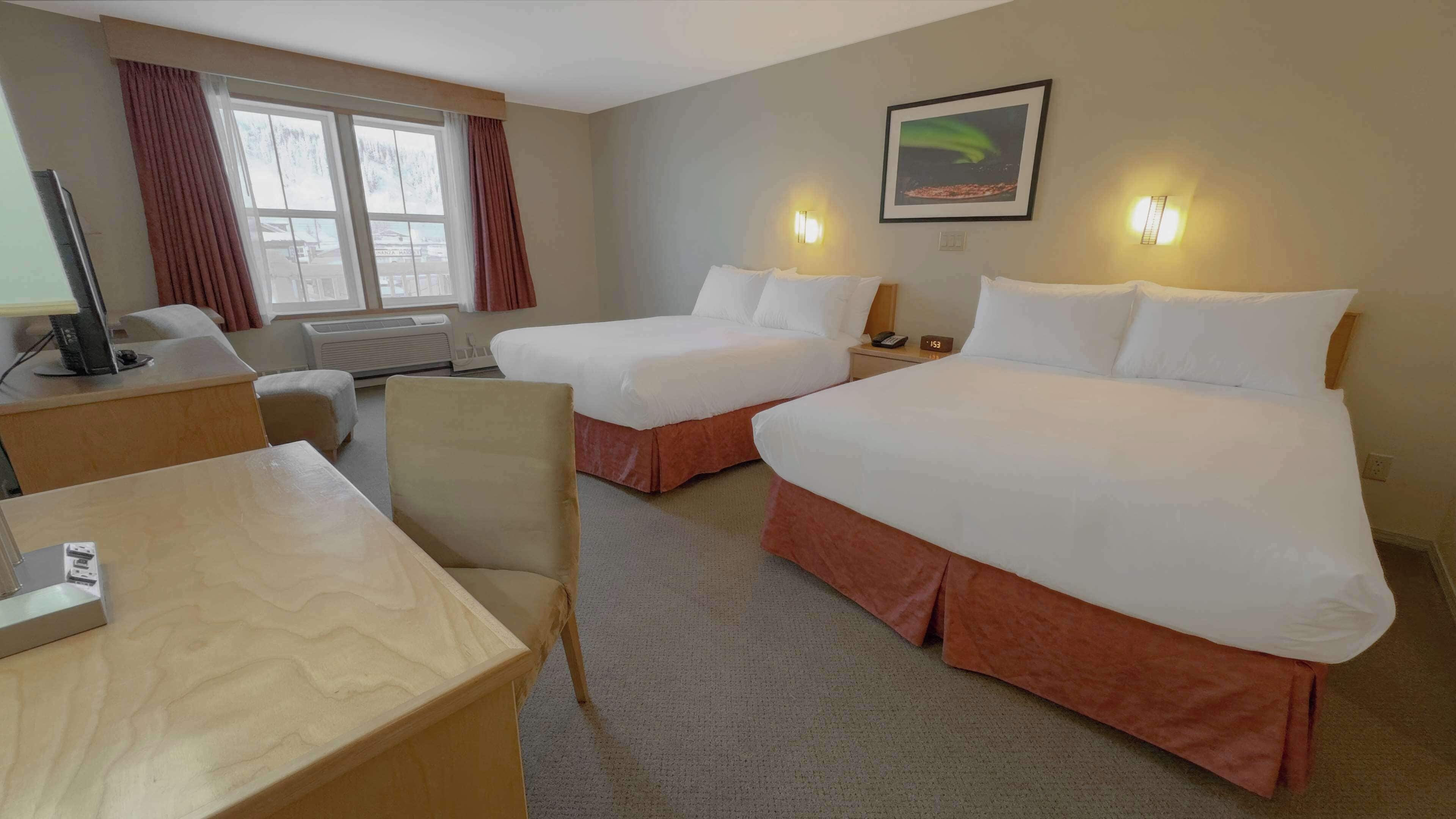 Ein Hotelzimmer mit zwei Betten, einem Schreibtisch, einem Stuhl, einem Fernseher und einem Fenster mit Vorhängen.