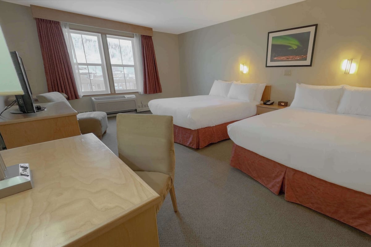 A hotel room with two beds, a desk, a chair, a TV, and a window with curtains.
