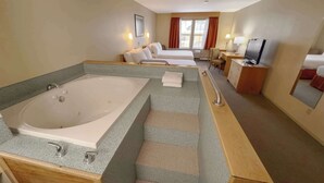 A hotel room with a large bathtub, a bed, a desk with a television, and a window with curtains. - Eldorado, a Coast Hotel (Dawson City)