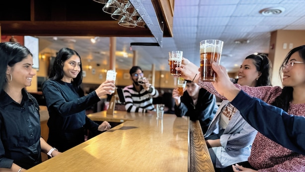 A group of people toasting with drinks at a wooden bar in a restaurant. - Eldorado, a Coast Hotel (Dawson City)