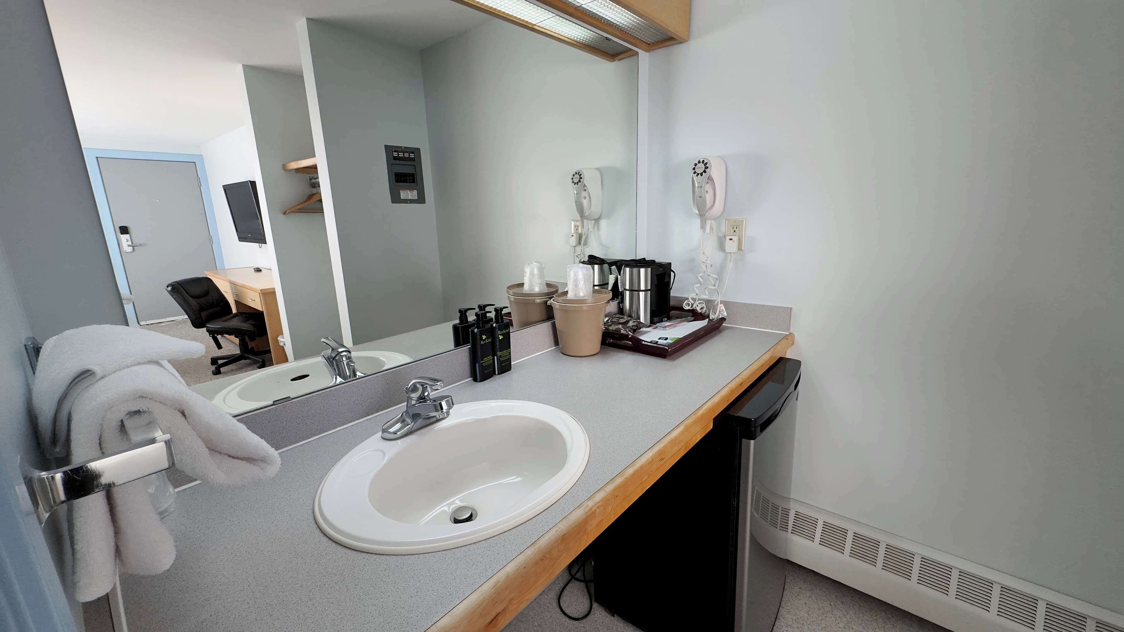 A bathroom with a sink, mirror, towel rack, and a coffee machine.