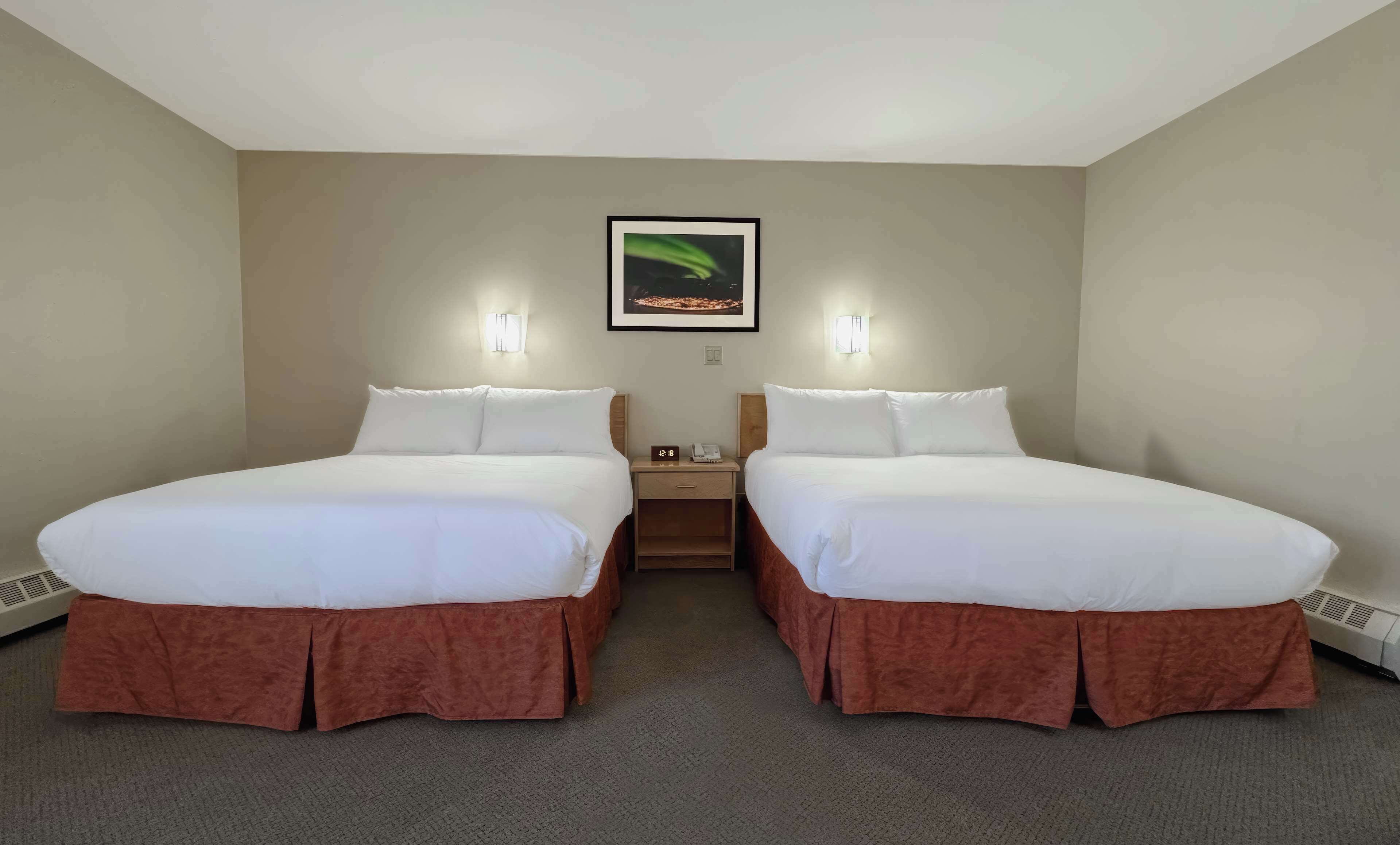 A hotel room with two beds, a nightstand, a framed picture on the wall, and a thermostat on the wall.