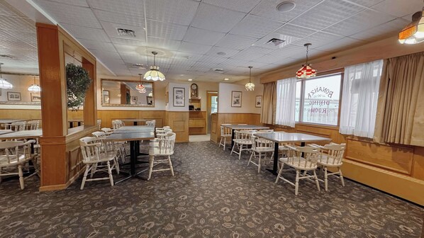 A restaurant with wooden paneling, white chairs, and patterned carpet.