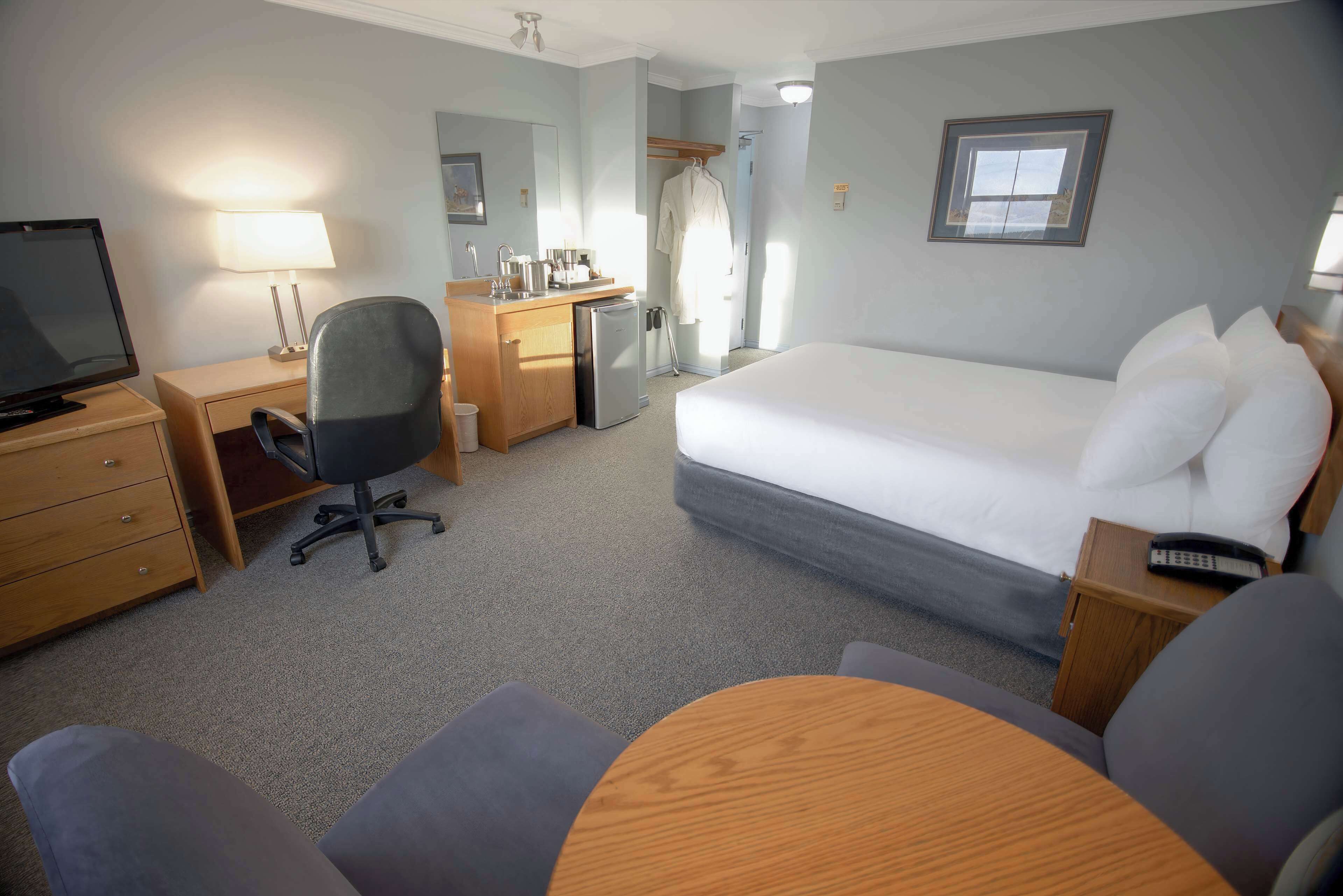 Ein Hotelzimmer mit Bett, Schreibtisch, Stuhl, Fernseher und kleinem Kühlschrank.