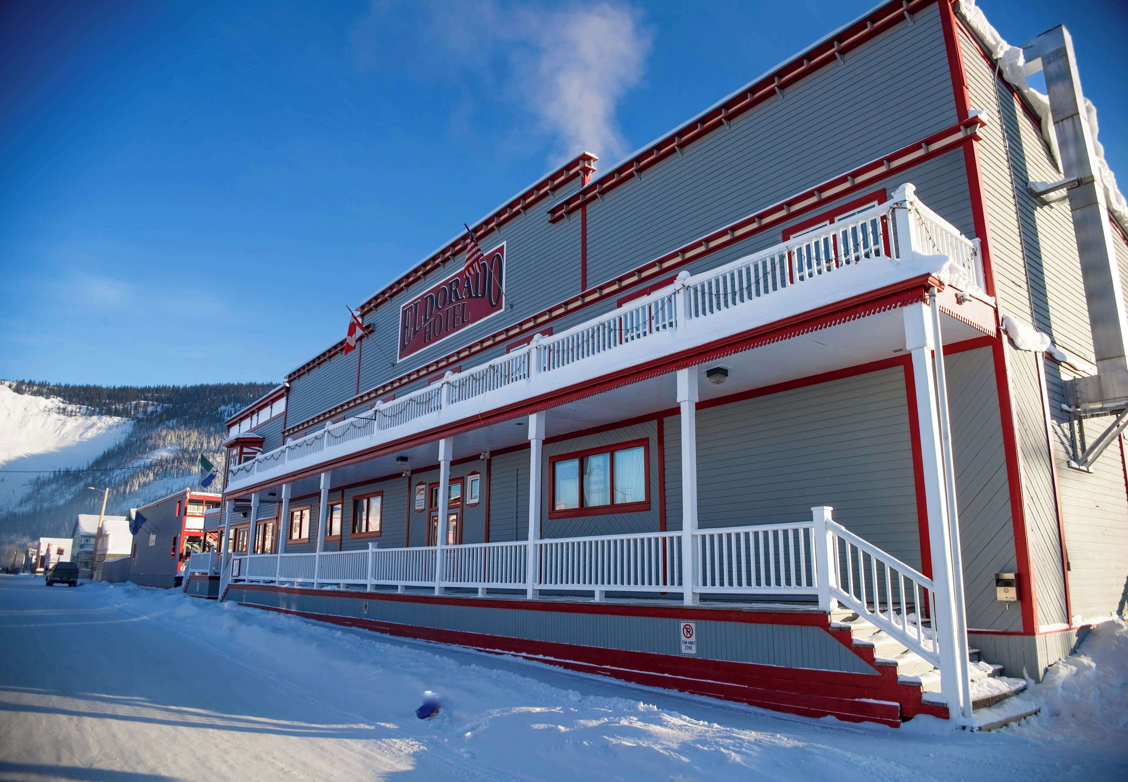 A hotel with a balcony, a staircase leading to the entrance, and a snowy landscape in the background.