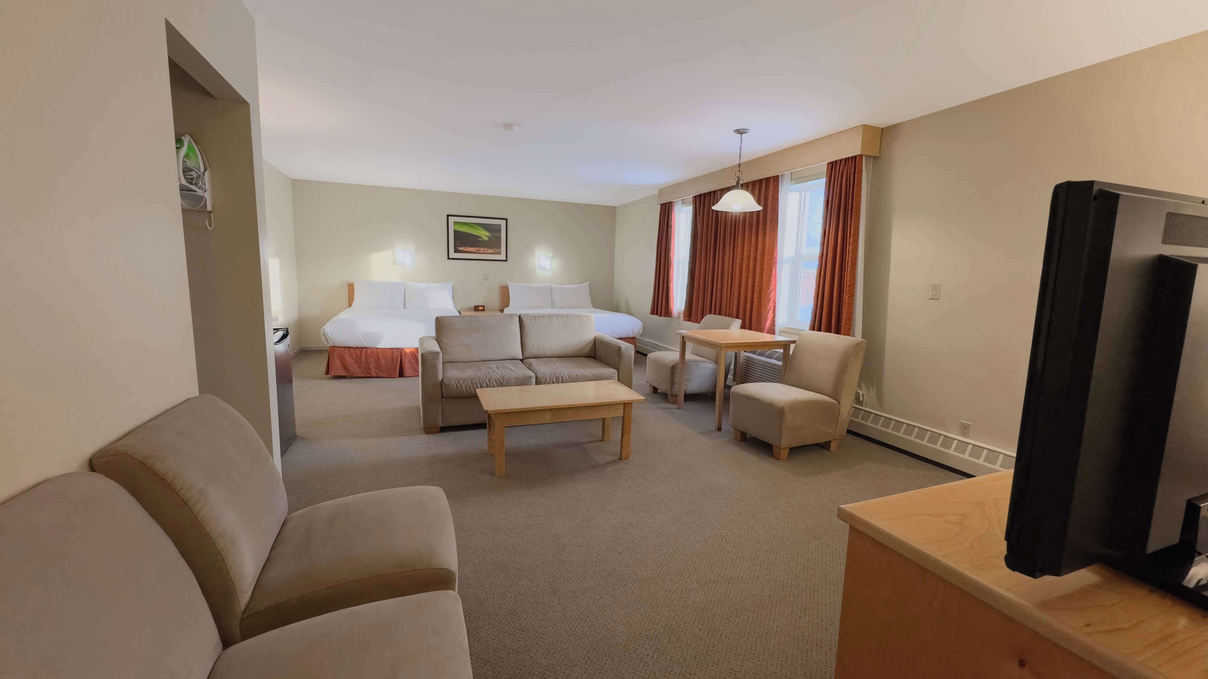 Ein Hotelzimmer mit einer Couch, einem Couchtisch, einem Fernseher, einem Bett und einem Schreibtisch.