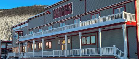 A hotel with a balcony, a sign reading 'ELDORADO HOTEL,' and a view of a forested mountain in the background.