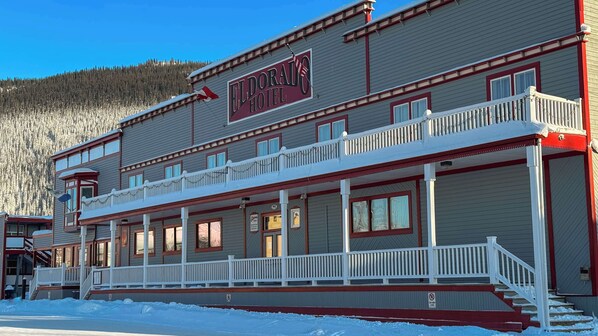 Un hôtel doté d’un balcon, d’une enseigne indiquant « HÔTEL ELDORADO » et offrant une vue sur une montagne boisée en arrière-plan.