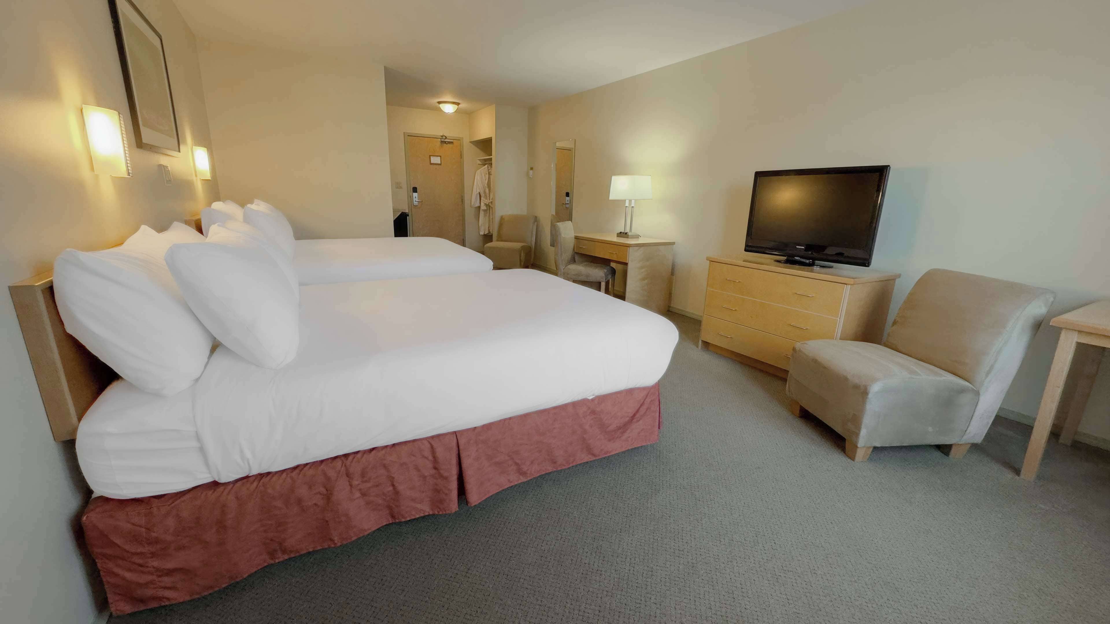 A hotel room with a large bed, a TV, a desk, and a chair.