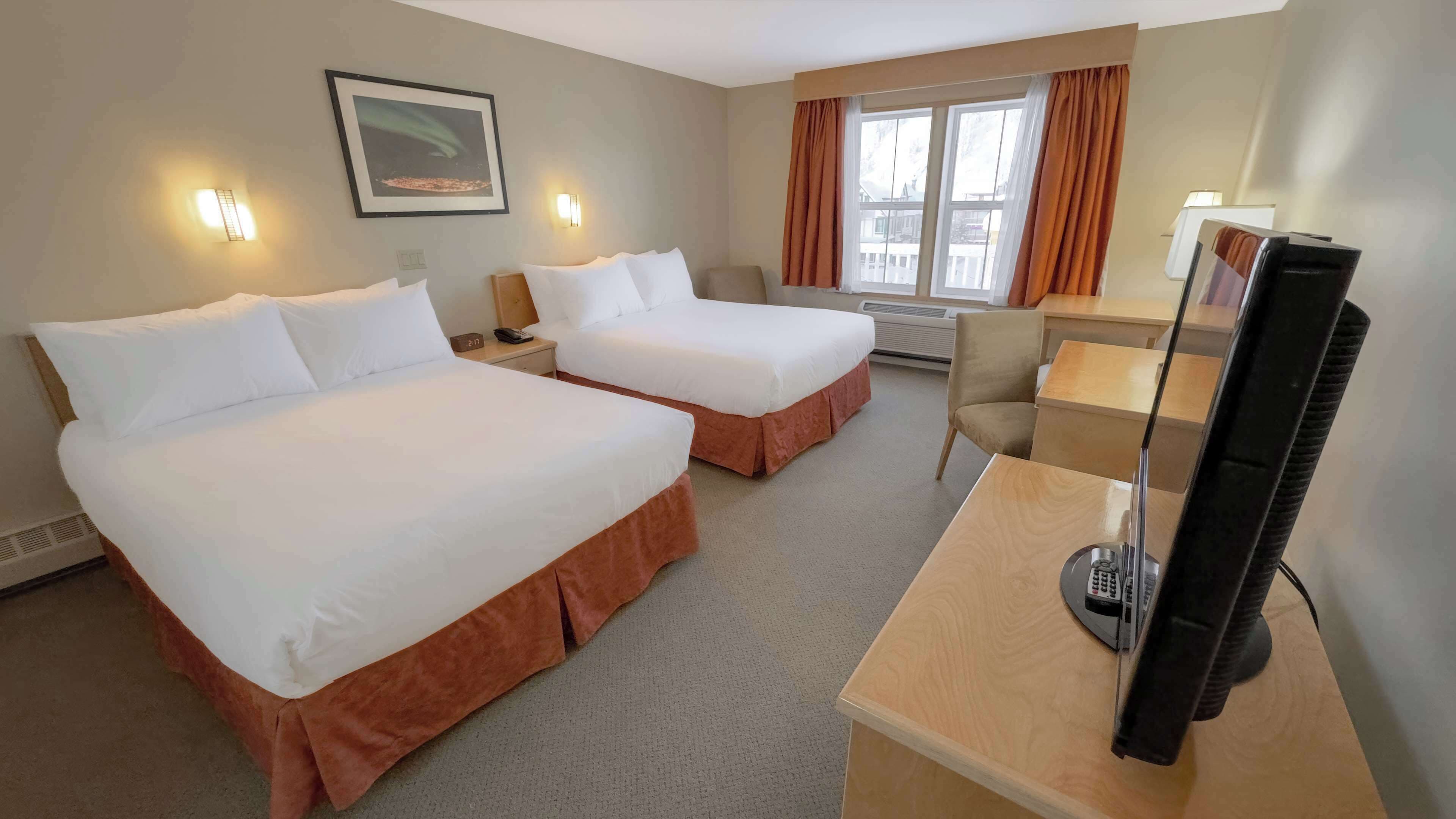 A hotel room with two beds, a desk with a television, and a window with curtains.