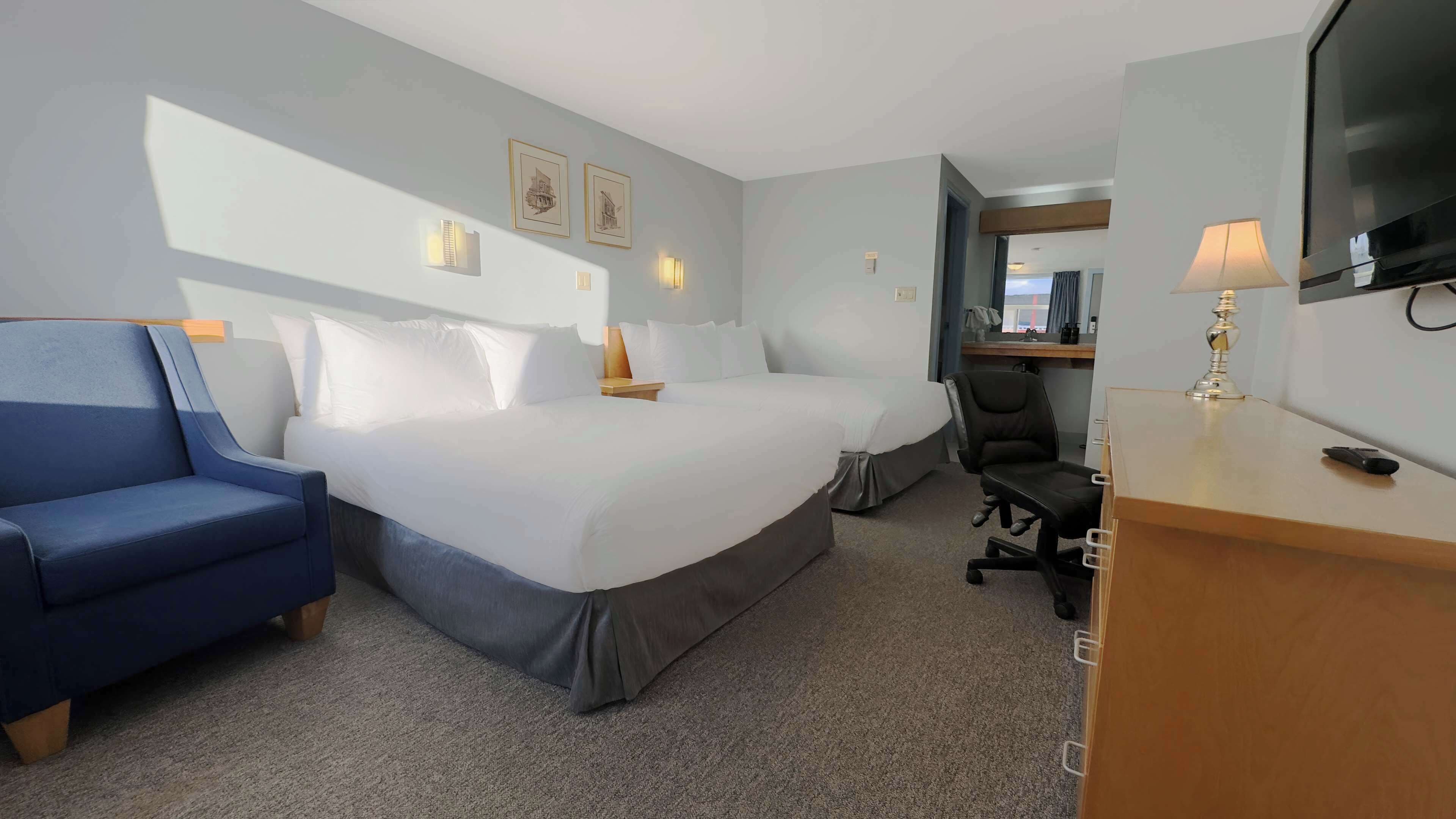 Ein Hotelzimmer mit einem großen Bett, einem Schreibtisch mit Lampe, einem Sessel und einem Fernseher.