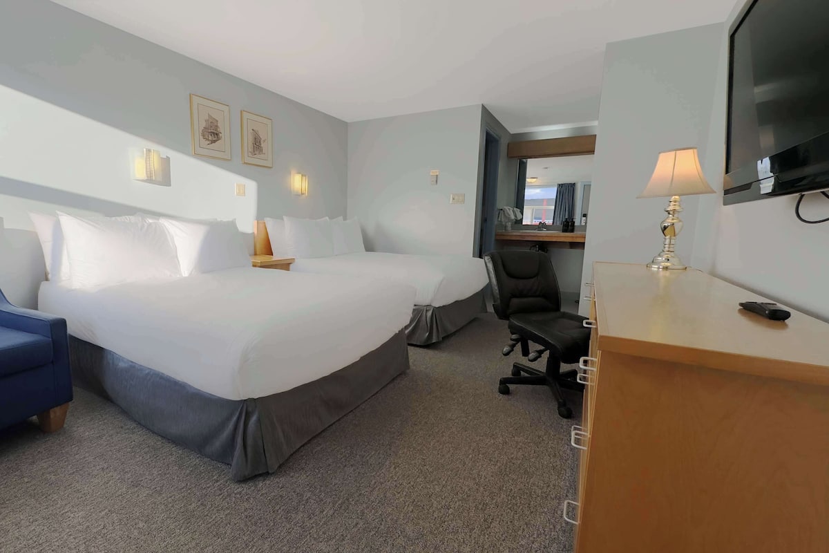 A hotel room with a large bed, a desk with a lamp, a chair, and a TV.