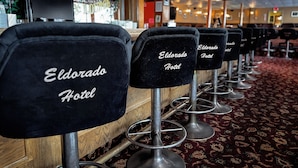 A row of bar stools with 'Eldorado Hotel' branding, a bar area, and a patterned carpet. - Eldorado, a Coast Hotel (Dawson City)