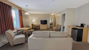 A hotel room with a sofa, a TV, a desk, a chair, a kitchenette, and a heater. - Eldorado, a Coast Hotel (Dawson City)