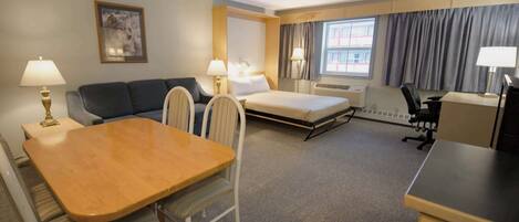 Habitación de hotel con cama, sofá, escritorio, silla, mesa, lámparas y ventana con cortinas.
