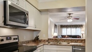 A kitchen with white cabinets, a microwave, stove, and dishwasher. There is a ceiling fan and a window with curtains. - Awesome Hilton Head Coligny Beach townhome! (Hilton Head Island)